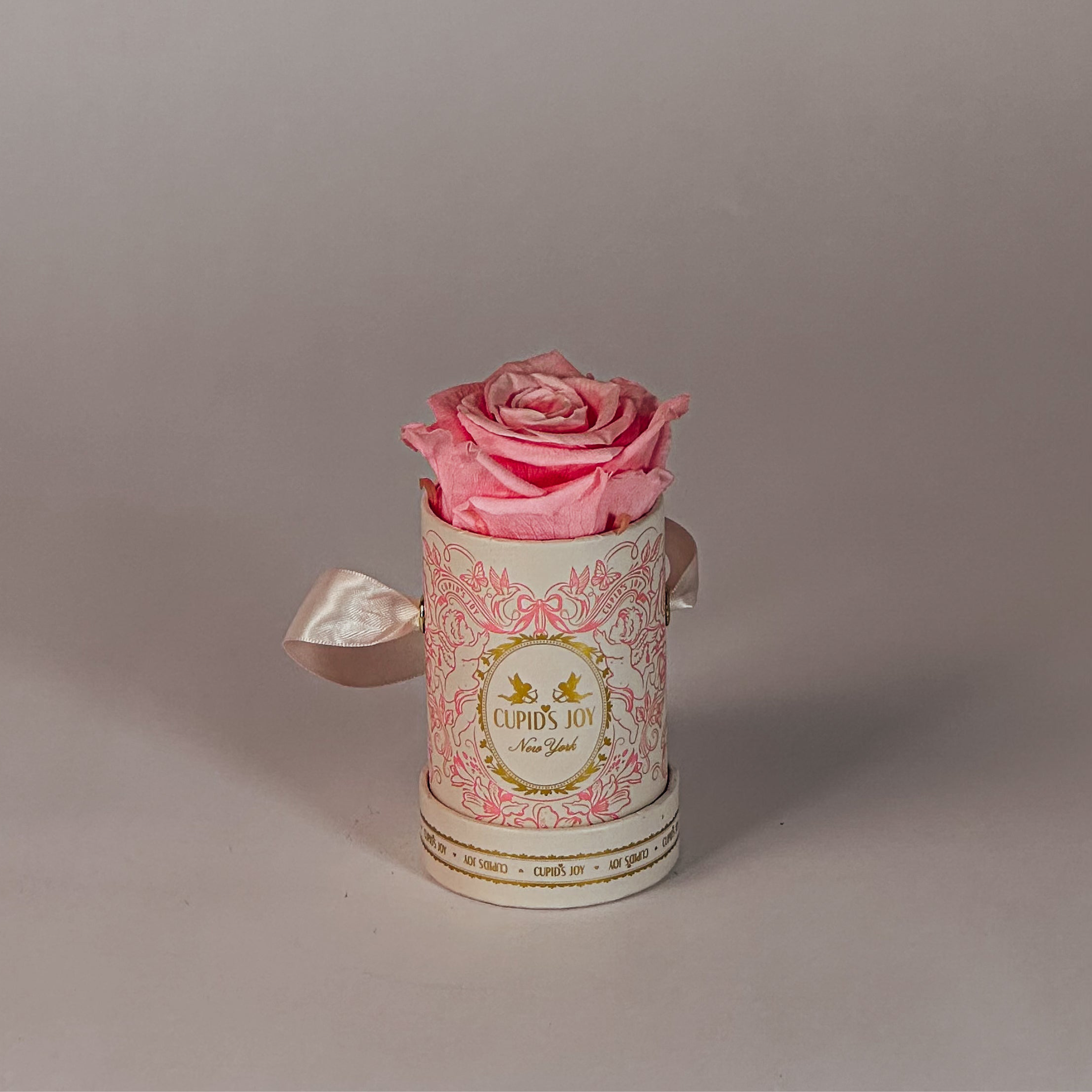 Pink rose in a hat box with Cupid's Joy logo on a gray background