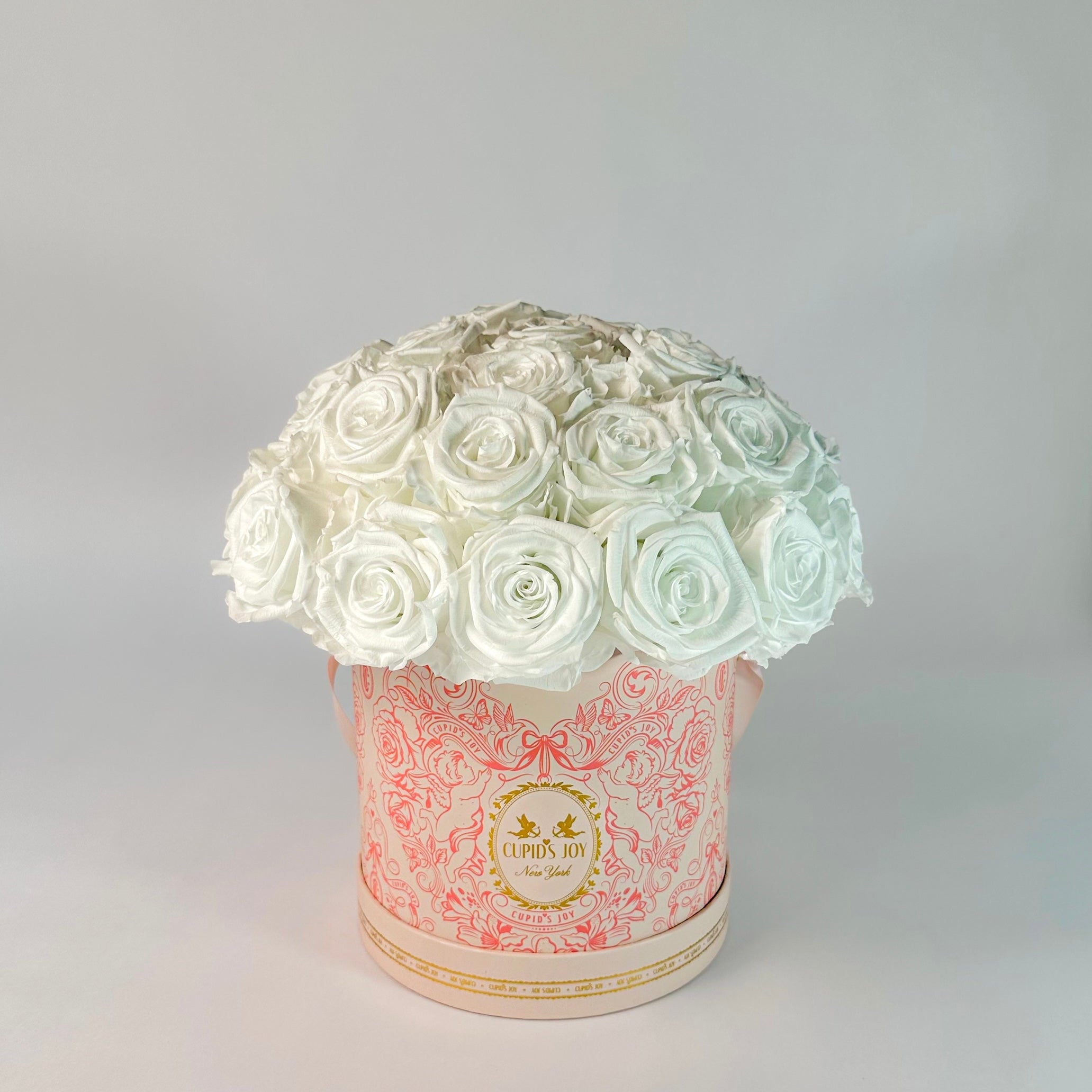 Round floral Rotunda Dome arrangement with white roses in a cupid-motif box on a light gray background